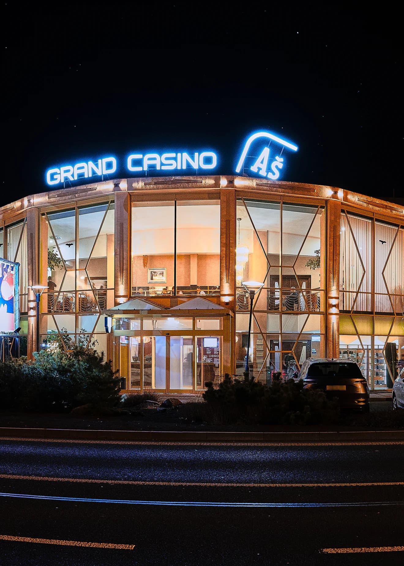 Budova Grand Casino Aš v noci s rozsvíceným modrým nápisem na střeše